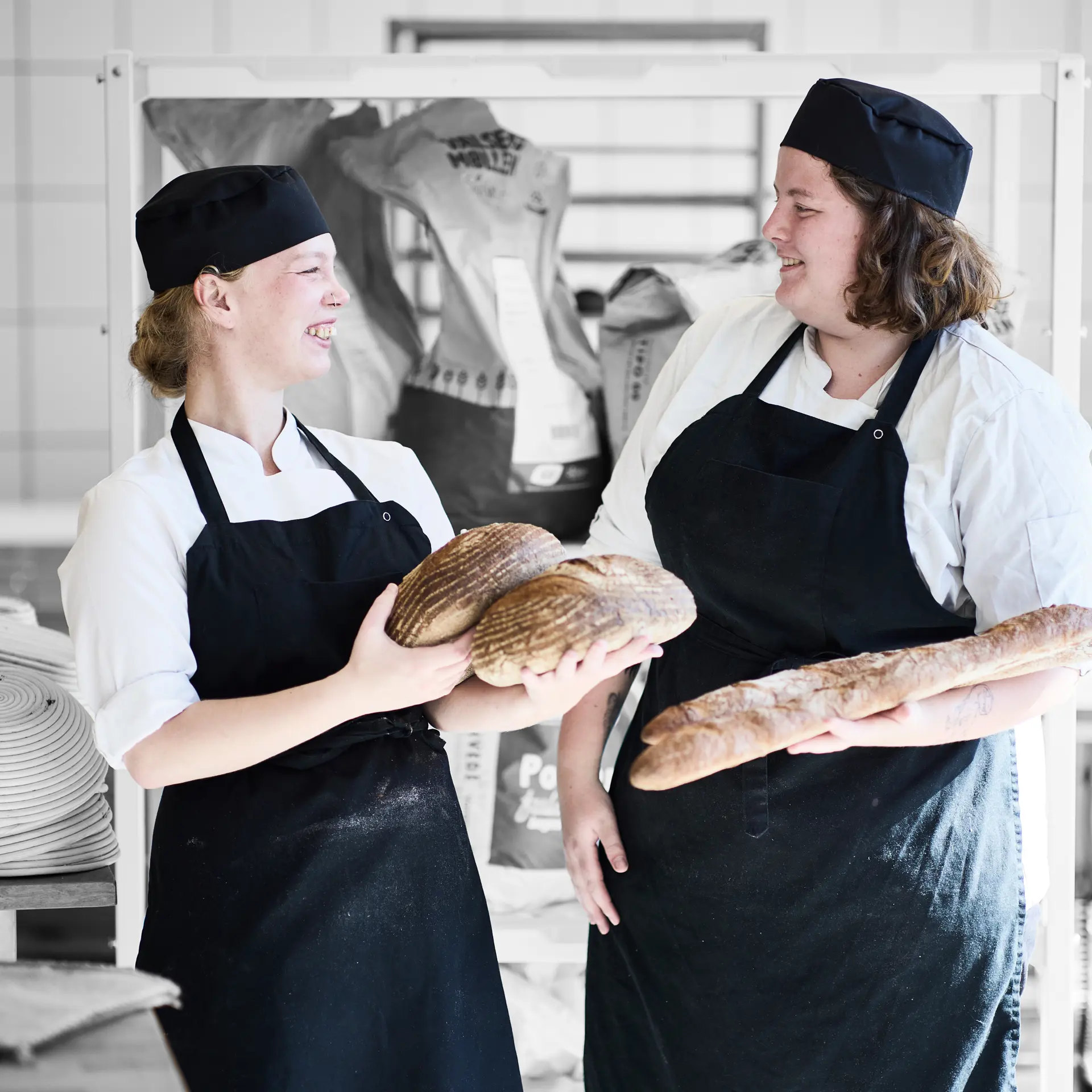 Bager smiler til hinanden, mens de står med brød i hånden