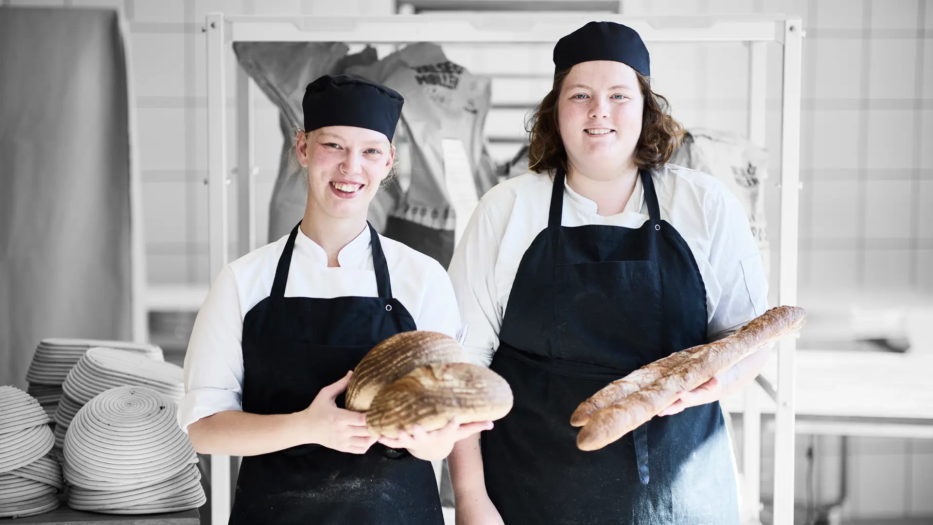 Bagere står med brød i hånden i et køkken